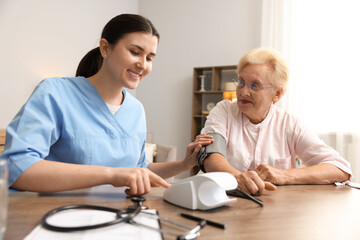 Fototapeta premium Nurse measuring patient's blood pressure at wooden table indoors. Home health care service