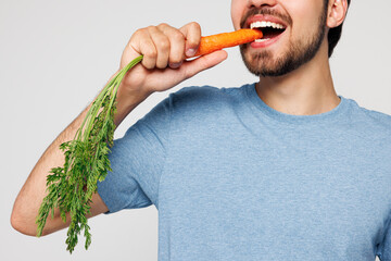 Close up cropped young man wear blue t-shirt casual clothes hold in hand eat bite carrot look...