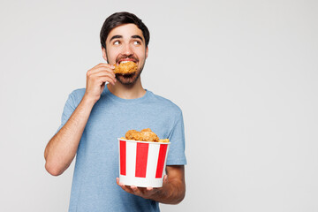 Young man wear blue t-shirt casual clothes hold takeaway box eat bite barbecue chicken meat wings...