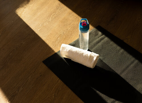 Fototapeta Black yoga mat is supporting white towel and water bottle with lid on floor in sunlight