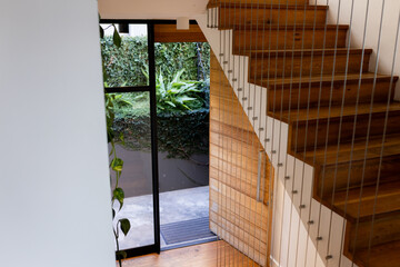 Floating wooden staircase with open treads and cable railing in entryway, revealing patio greenery