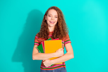 Cheerful young woman holding colorful notebooks against turquoise background showcasing fun style...