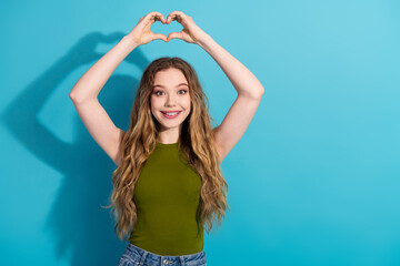 Happy young woman making a heart shape with hands on blue background, expressing love, positivity,...