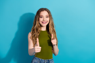 Cheerful young girl pointing with both hands while smiling against a vivid solid blue background.