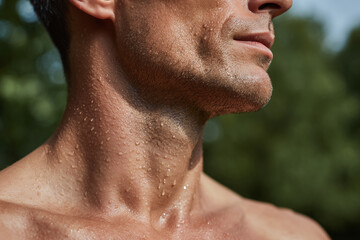 Naklejka premium Close up of man jawline and neck covered with water droplets, showing smooth skin texture and subtle facial hair in natural outdoor light, evoking freshness and vitality