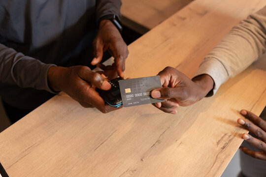 African American male clerk and customer exchanging payment on card reader at cafe service counter