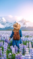 A woman in a flowing blue dress and wide-brimmed hat strolls gracefully through a vibrant field of colorful wildflowers, basking in the sunlight.