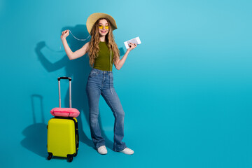 Fashionable young woman in stylish travel outfit holding a boarding pass on blue background with...