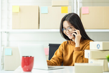 Young Asian woman, a small business owner, working from home. Happy female entrepreneur managing her online store, checking orders on laptop, and confirming shipment details.