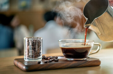 black drip espresso crema foam coffee in glass cup, Barista making drip coffee by pouring spills hot water on coffee bean. Barista serve cup of hot black coffee or americano on wooden table cafe shop