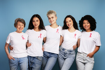 Diverse women wearing pink ribbons are embracing for breast cancer awareness