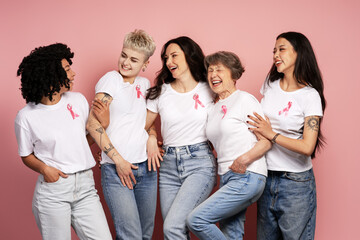 Diverse women laughing and supporting breast cancer awareness, wearing pink ribbons