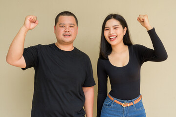Portrait of young couple against plain wall background with fist raised