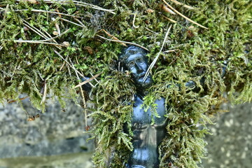 Close-up of a moss-covered metallic cross embedded in a stone wall.A Study in Texture and Nature
