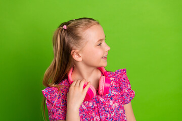 Joyful young girl wearing pink floral dress with headphones poses against a vibrant green...