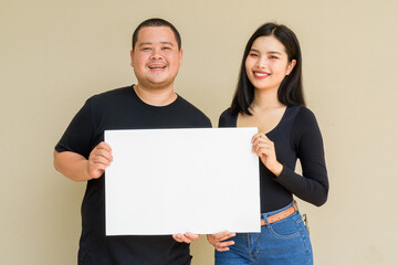 Portrait of young couple against plain wall background holding placard with copy space