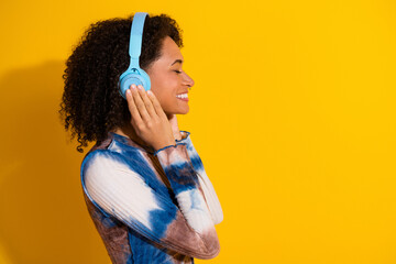 Young woman enjoying music with blue headphones against vibrant yellow backdrop, wearing stylish...
