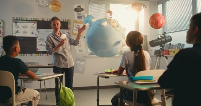 Female Teacher Educating Smart Kids During Science Lesson in Multiethnic Classroom. Primary School Boy Presenting Green Energy Sources in Front of Class Using Earth Model. STEM Education. Dolly Shot. - Powered by Adobe