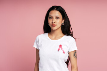 Young woman wearing pink ribbon supporting breast cancer awareness on pink background