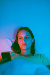 Teen girl lying in bed illuminated by phone screen glow at night
