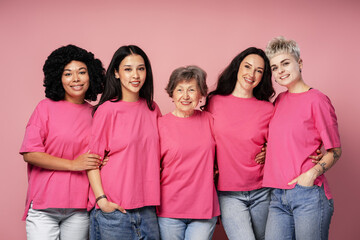 Five women of different ages and ethnicities embracing and wearing pink t shirts
