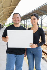 Young couple in train station together holding placard