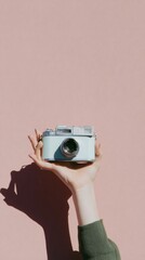 A hand holds a vintage camera against a pastel pink background. The scene evokes feelings of nostalgia and minimalism, highlighting retro aesthetics.