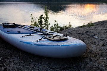 Inflatable paddle board on lake shore at sunset