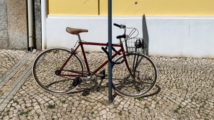 A rust-red bicycle leans nostalgically on a sunlit cobblestone, whispers of slow travel, and World...