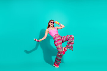 Stylish woman in vivid retro attire dancing and posing against a bright turquoise background in a...