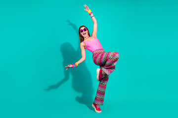 Energetic young woman in retro fashion outfit posing on teal background showcasing dynamic...