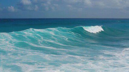 Turquoise ocean wave crashing under a blue sky, showcasing nature's raw power and beauty.