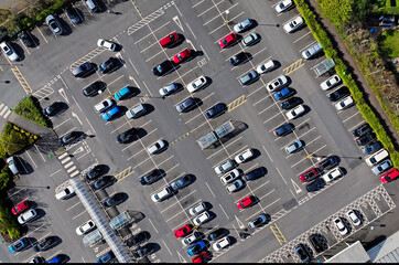 Aerial drone view of multiple coloured cars and vehicles parked in white painted spaces in a large...
