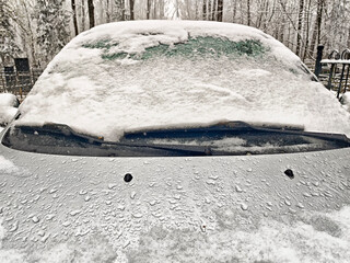Snow-covered car parked in a winter landscape surrounded by trees on a cold day