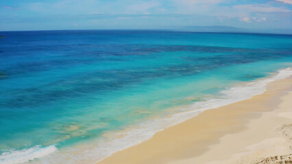 Aerial view of a pristine beach with turquoise water and white sand under a clear sky.