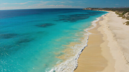 Aerial view of a tropical beach with turquoise water and golden sand on a sunny day.