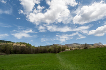 Amazing green meadow in the mountains. Meadow covered with blue sky filled with white fluffy clouds. Spring nature photography.