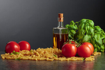 Fusilli pasta with olive oil, tomatoes and basil on a black background.