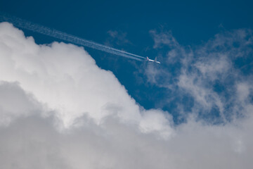 Airplane flies among bizarre clouds in blue sky