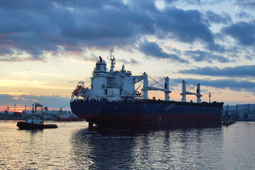 Two small service boats escort a large cargo ship into dock