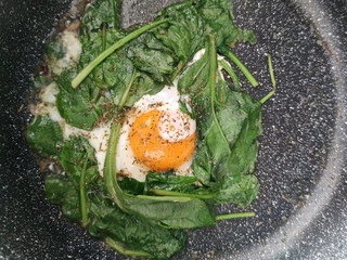 Scrambled eggs with spinach on a granite frying pan close-up from above