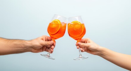 Two hands clinking glasses filled with refreshing aperol spritz cocktails topped with orange slices in a celebratory toast