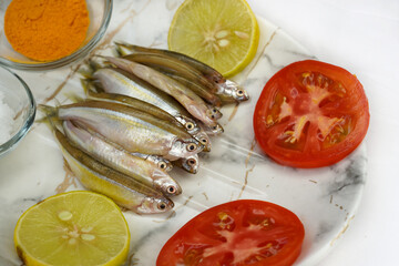 Fresh raw fish smelt or sardines ready for cooking with lemon, tomatos and salt. The concept of...