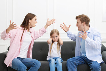 Upset little girl and her parents fighting on sofa at home