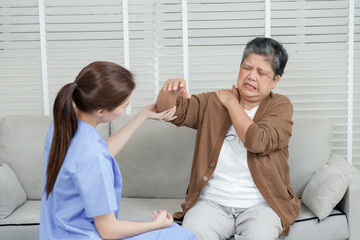 Asian female physiotherapist gently holding arm of senior asian woman pointing to painful shoulder during physical therapy consultation in private rehabilitation room with white blinds