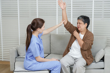 Obraz premium Senior asian woman lifting arm as female physiotherapist supports hand gently during muscle recovery and shoulder mobility training in orthopedic therapy session in peaceful clinic space