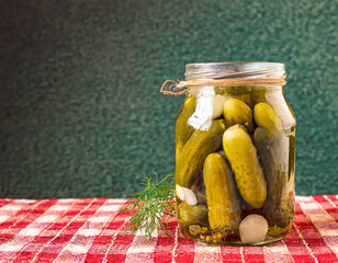 A jar of pickles sits on a table. The pickles are green and are arranged in a way that they look like they are ready to be eaten