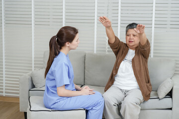Elderly asian woman raising hands upward while performing stretching exercise guided by female...