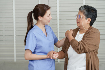 Asian female physical therapist gently supports senior asian woman during arm rehabilitation...