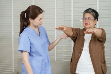Senior asian woman practices shoulder extension movement guided by asian female physiotherapist during physical rehabilitation session for upper body training at indoor clinic